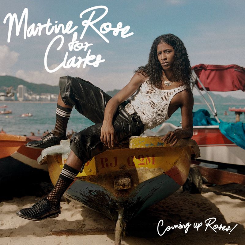 Editorial fashion shot of a female model sitting on a yellow and blue boat with a coastal city and ocean background.