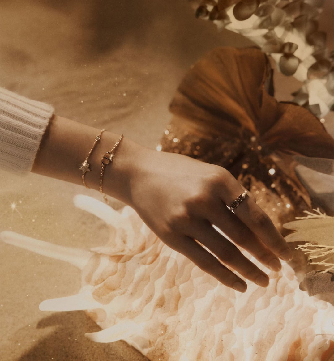 Close-up of a person wearing gold bracelets and a ring, resting a hand near a large seashell.