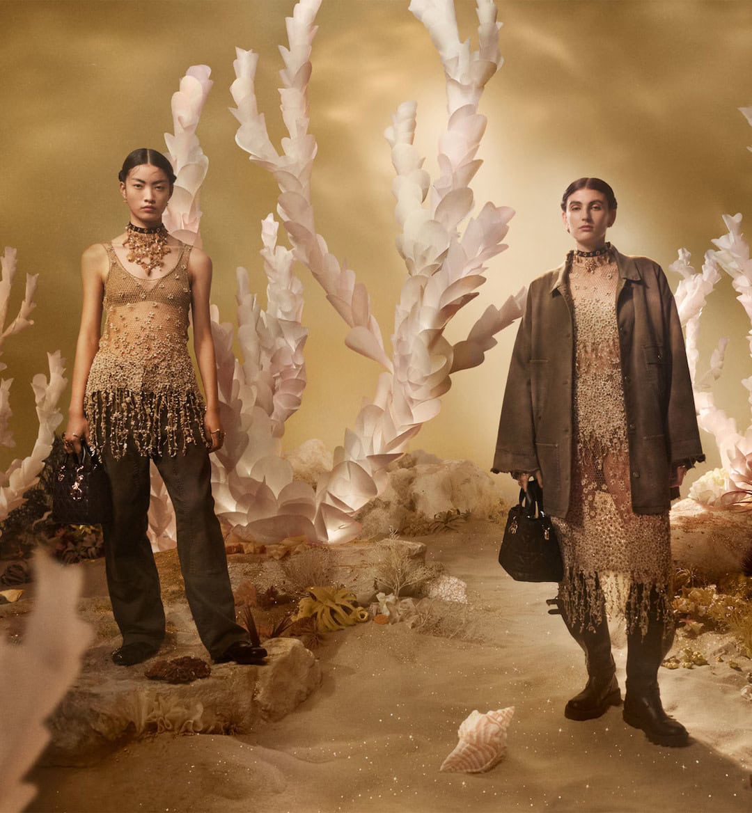 Two female models posing in an underwater coral setting wearing Dior Holiday 2024 campaign apparel.