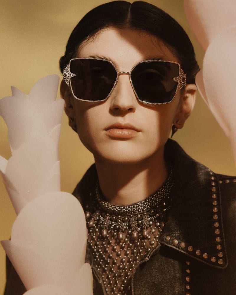 Model wearing dark sunglasses with embellished frames and a studded jacket in a campaign shot by Agnes Lloyd-Platt for Dior.