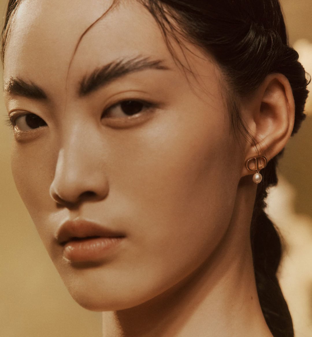 Close-up portrait of an East Asian model wearing gold CD earrings with pearls for Dior Holiday 2024 campaign