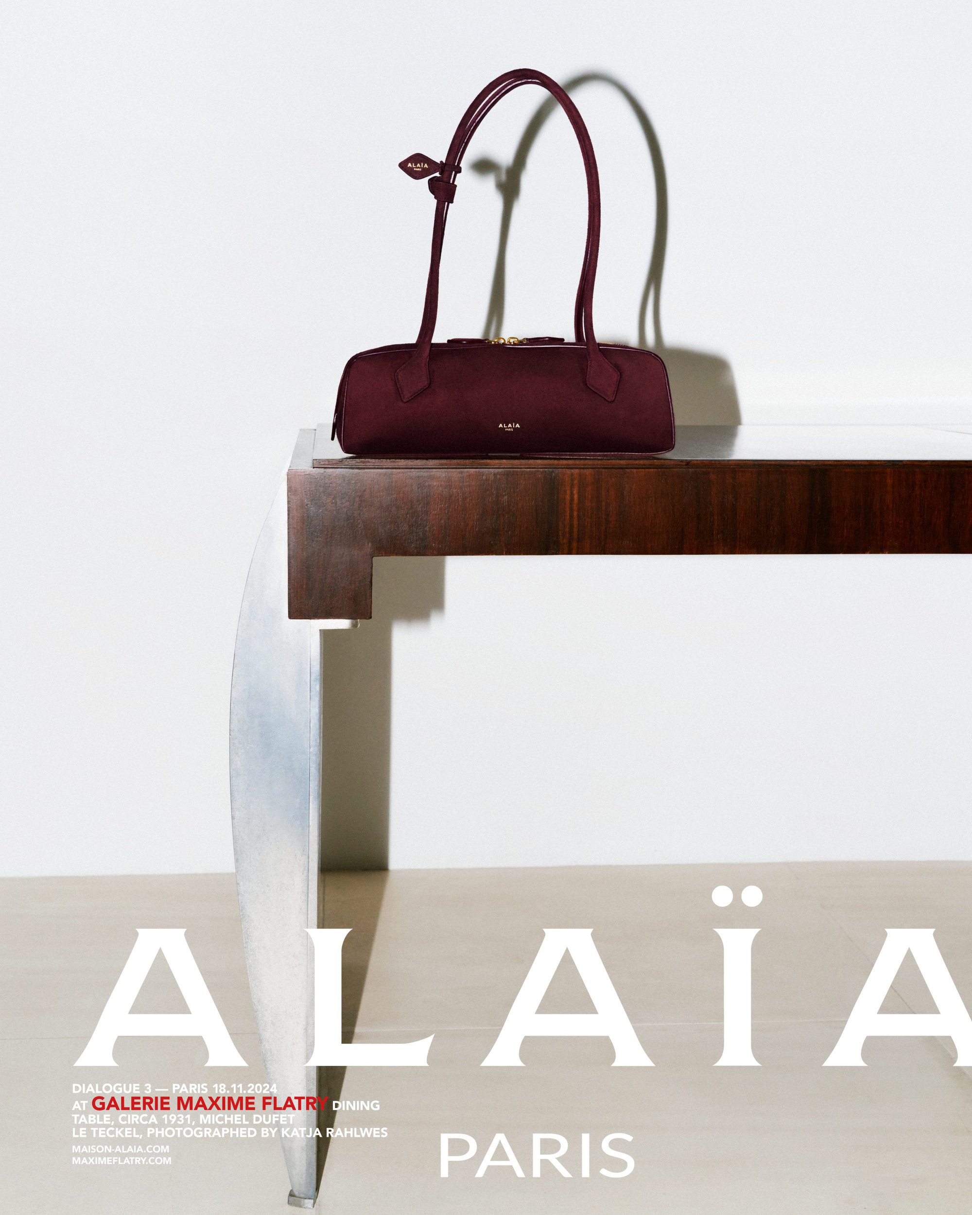 Burgundy leather handbag with long dual straps resting on a dark wood and metallic console table against a white wall.