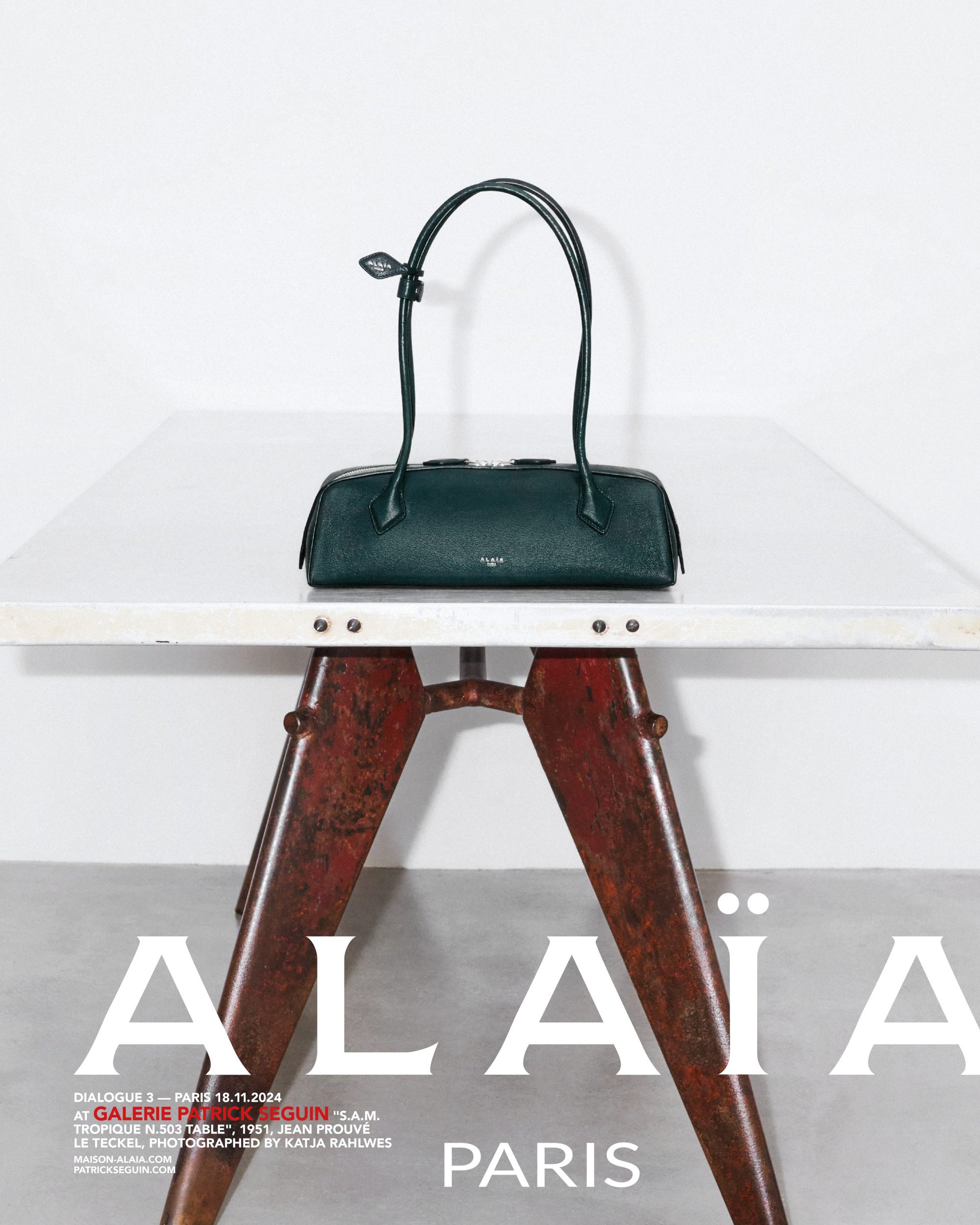 Dark green leather handbag resting on a white-topped metal table against a white wall.