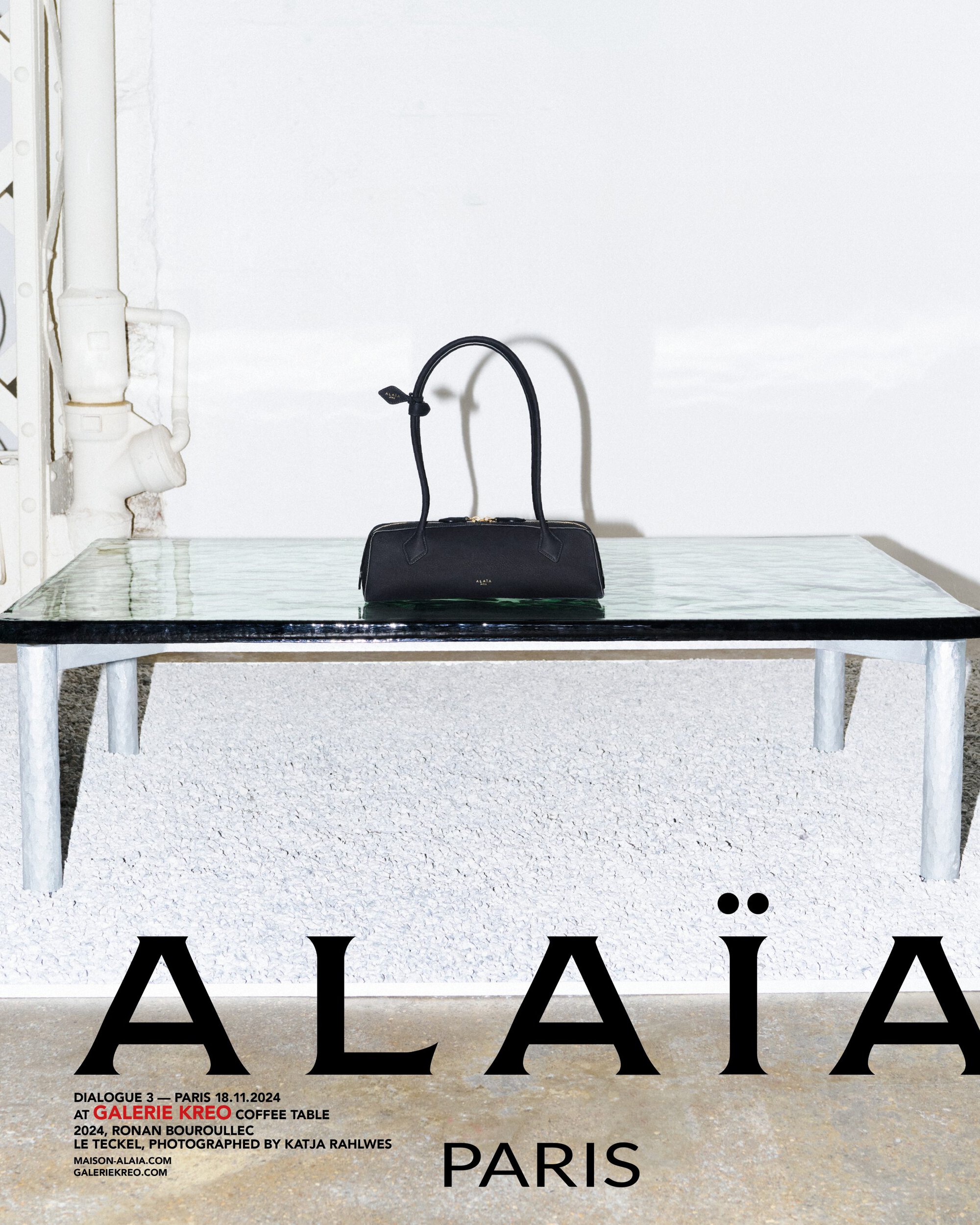 Black cylindrical handbag resting on a glass coffee table in an interior setting for Alaia Fall 2024 campaign