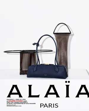 A dark blue leather shoulder bag displayed alongside two woven vessels against a white background with prominent bold black typography.