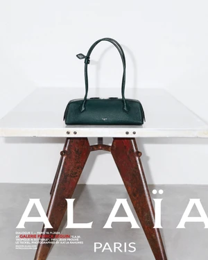 Dark green leather handbag resting on a white-topped metal table against a white wall.