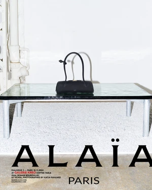 Black cylindrical handbag resting on a glass coffee table in an interior setting for Alaia Fall 2024 campaign