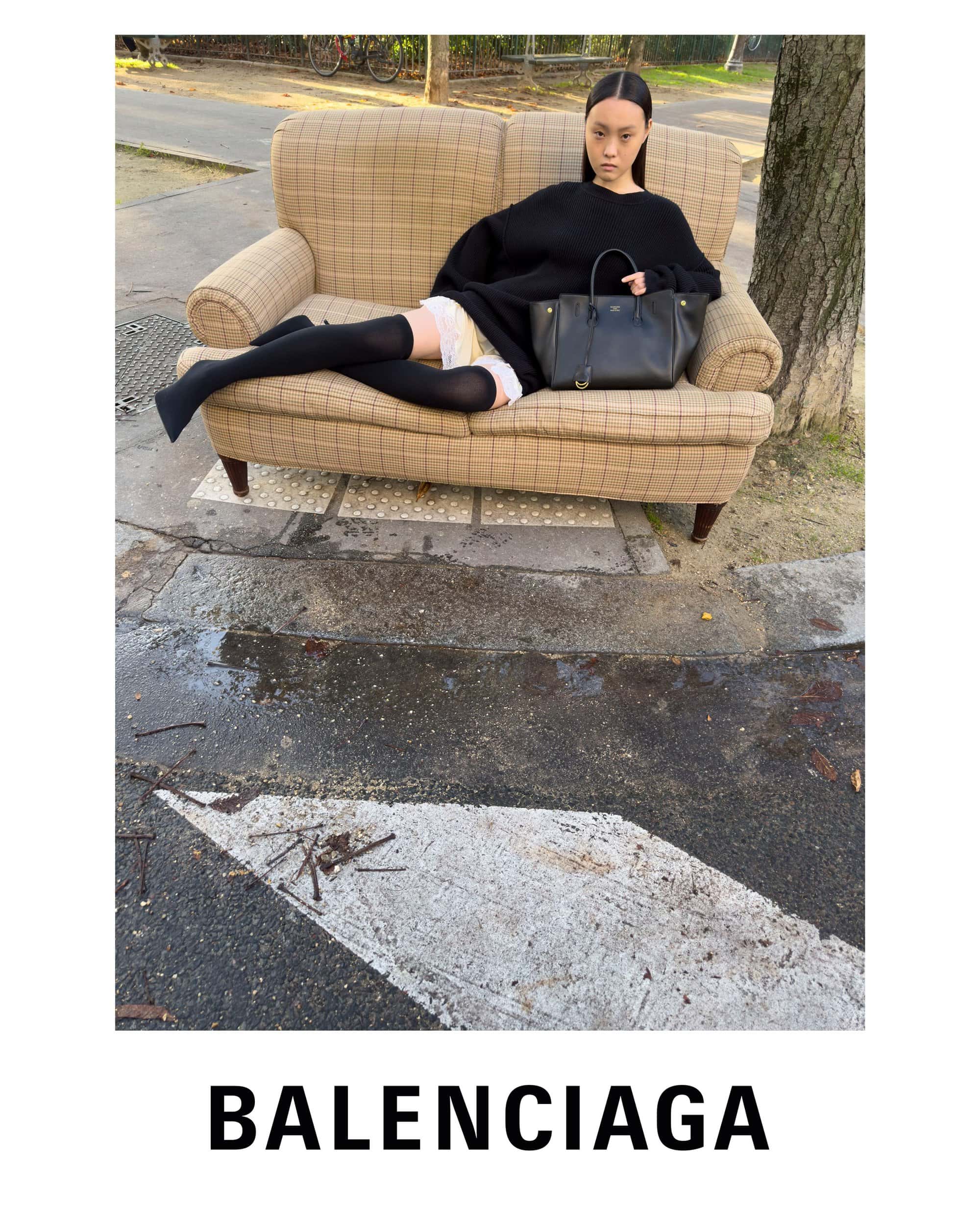 Model lounging on a plaid sofa outdoors with a black handbag in a Balenciaga campaign photographed by Juergen Teller.