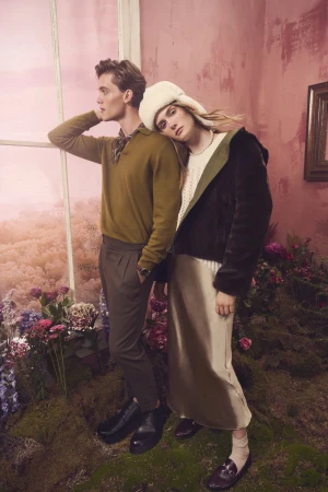 A man in a green sweater and a woman in a fluffy white hat posing together in a rosy interior room for the RW&CO. Holiday 2024 campaign.