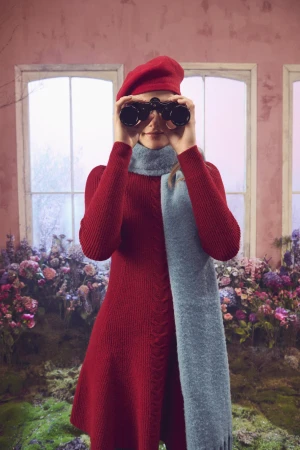 Woman in a red dress and beret holding binoculars to her eyes, wearing a light blue scarf.