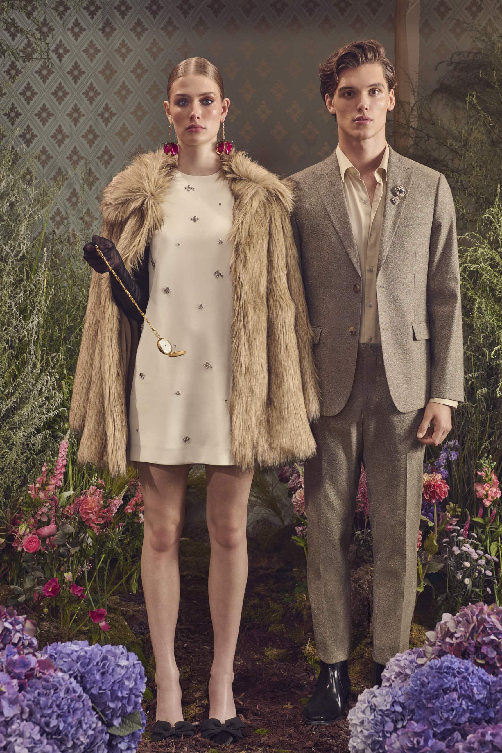 A man and a woman posing together amidst lush purple flowers and a patterned backdrop for an RW&CO. holiday campaign.