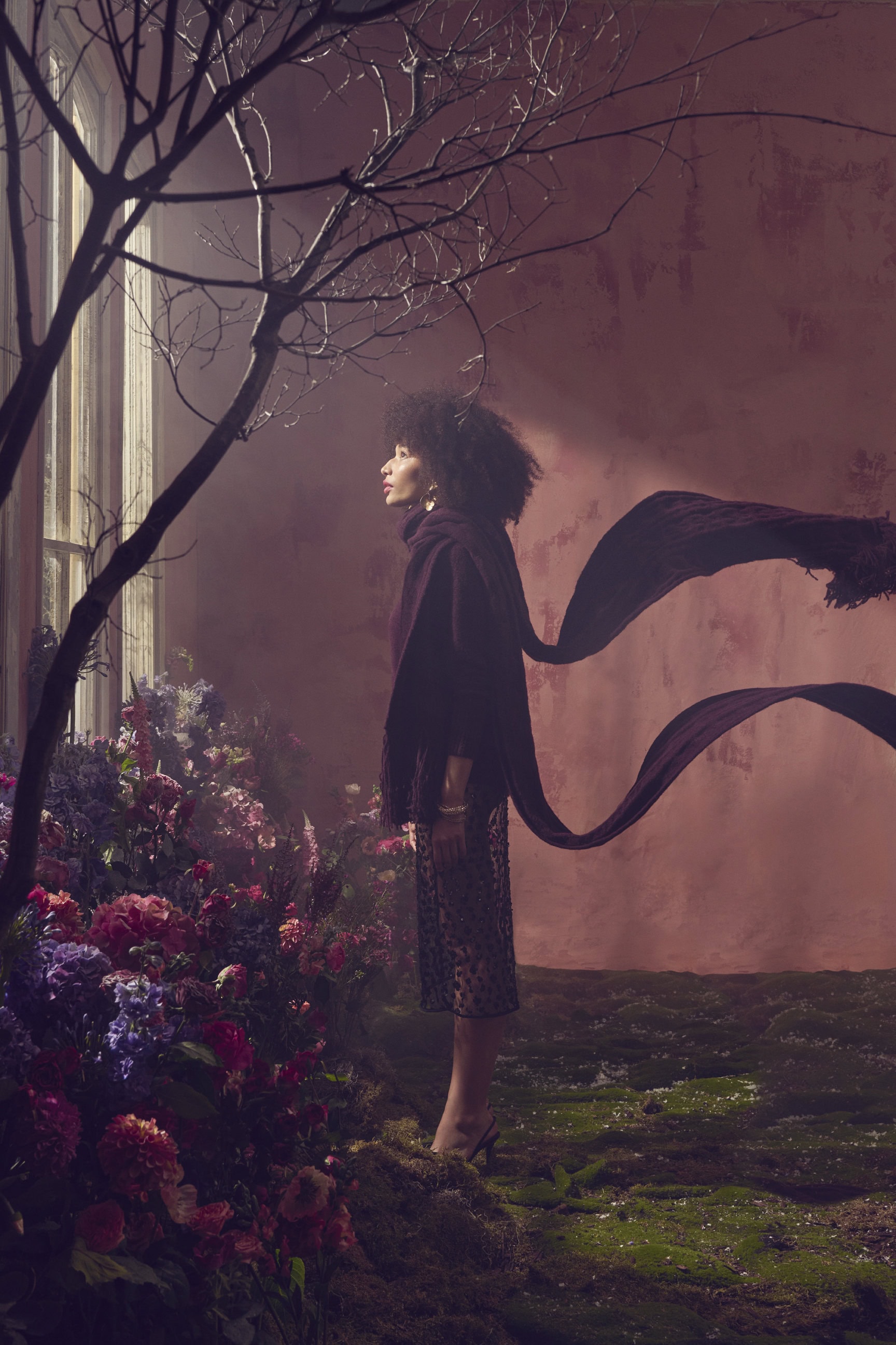 Woman in dark turtleneck and sheer skirt standing among flowers near a window for RW&CO.