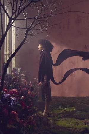 Woman in dark turtleneck and sheer skirt standing among flowers near a window for RW&CO.