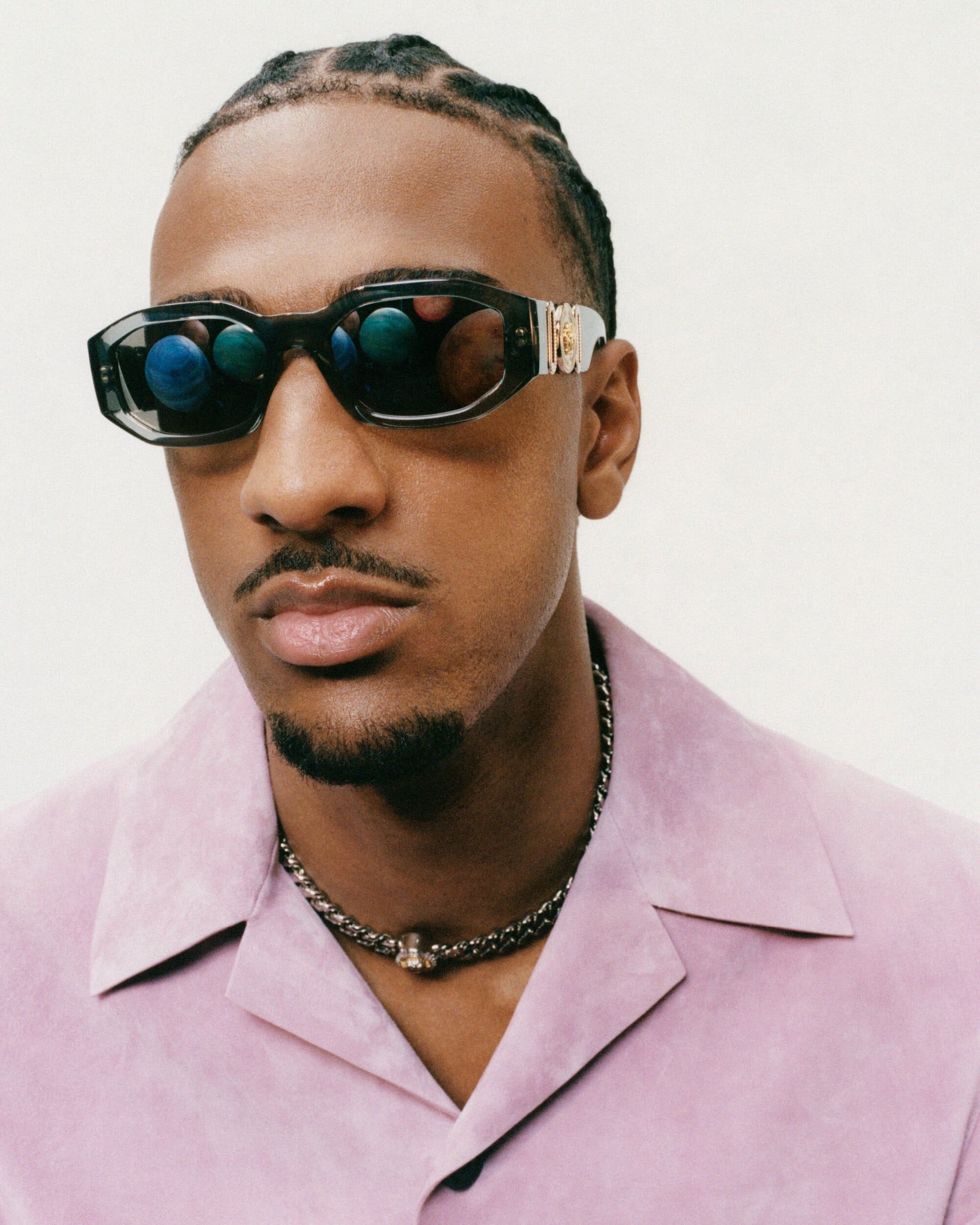 Man wearing dark sunglasses and a pink collared shirt against a white background for the Versace Medusa Biggie campaign.