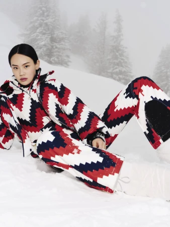 Model in red white and blue patterned ski suit posing on snowy slope in winter
