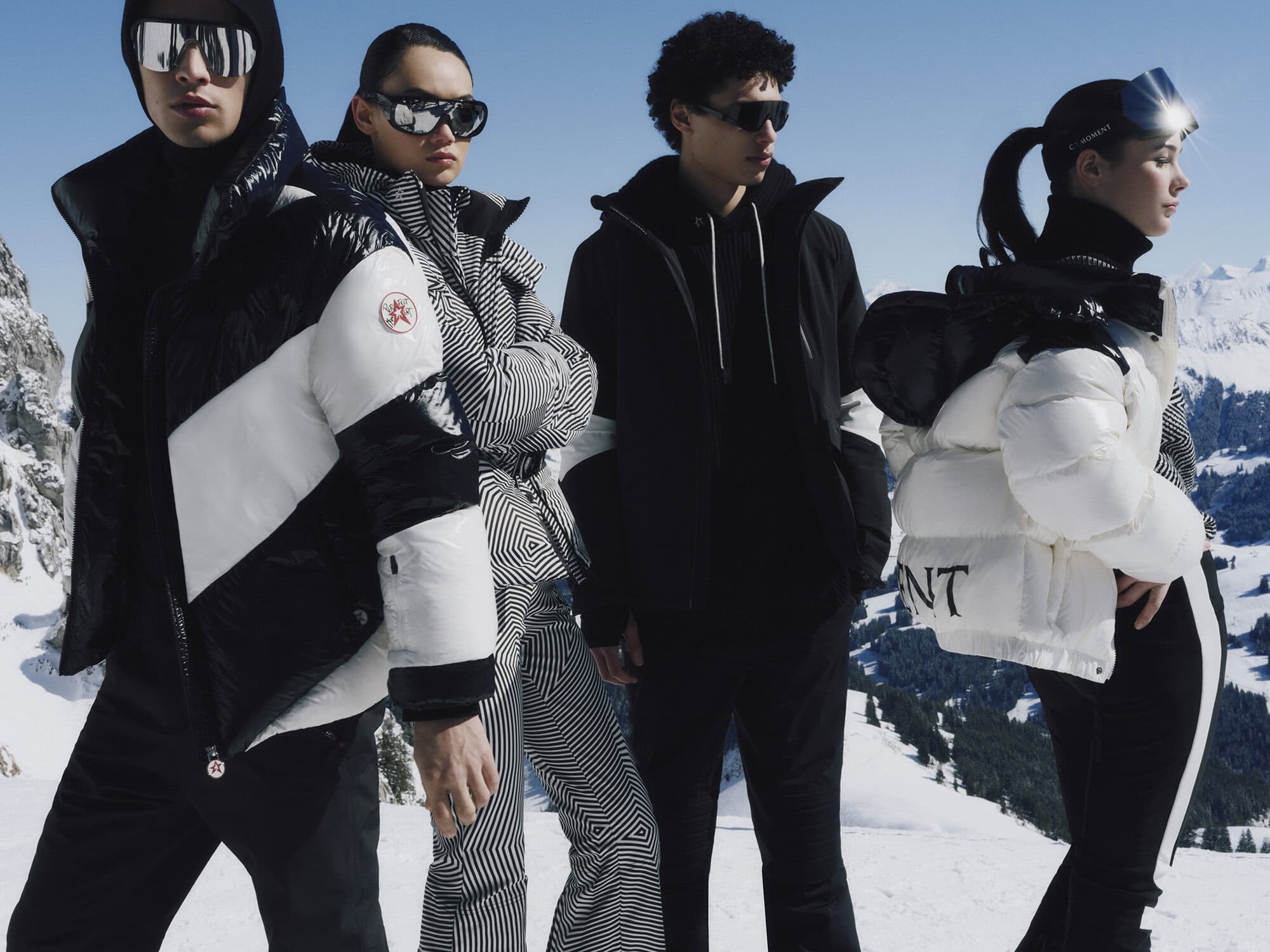 Four models in winter outerwear and sunglasses posing outdoors against a snow-covered mountain backdrop.