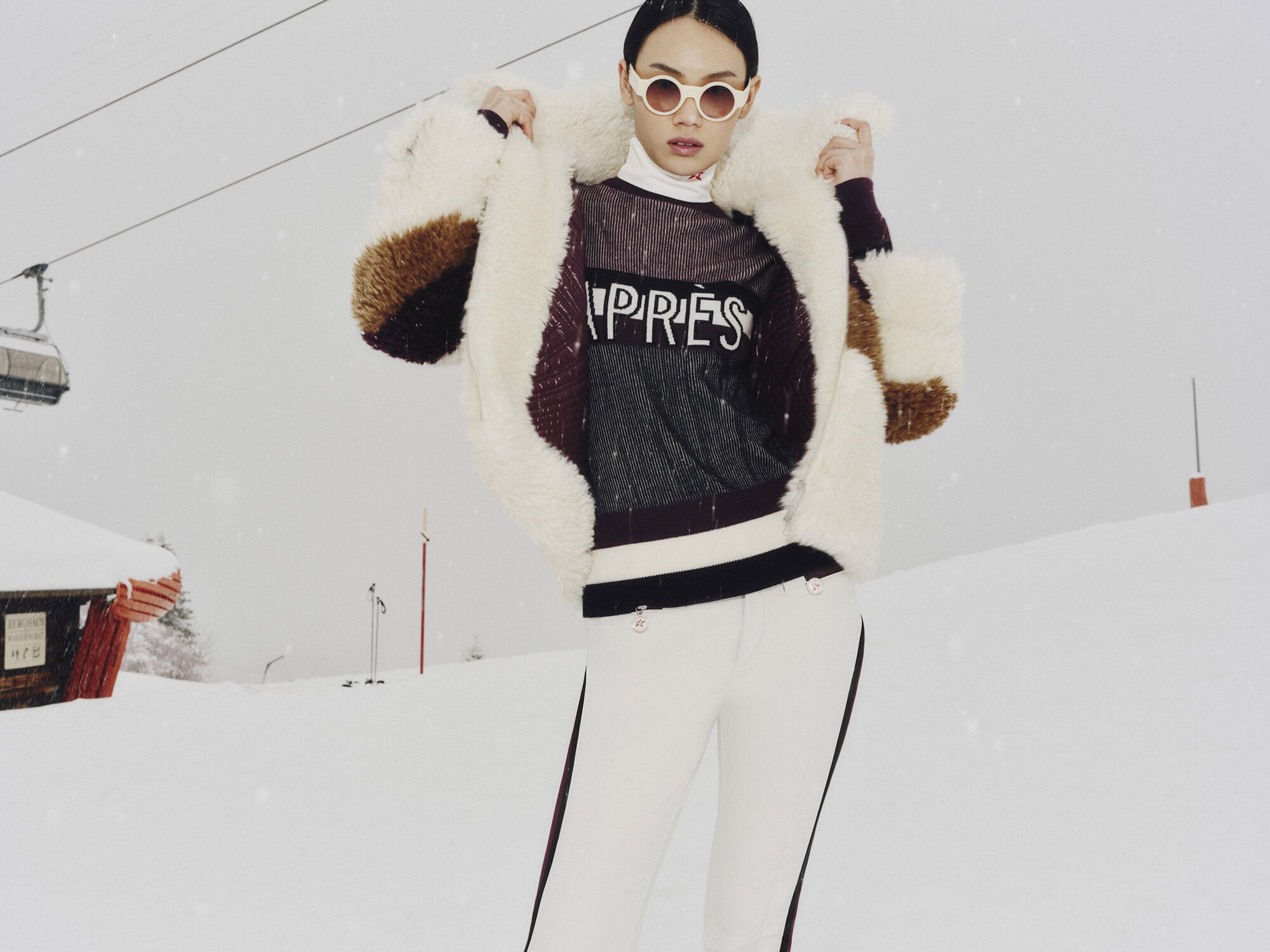Model wearing a shearling coat and white sunglasses on a snowy ski slope