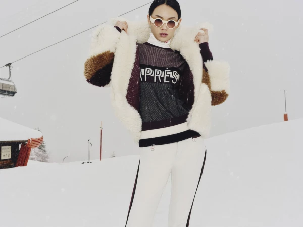 Model wearing a shearling coat and white sunglasses on a snowy ski slope