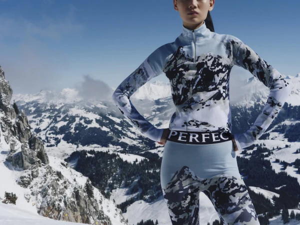 Model wearing mountain-print athletic apparel standing against a snowy mountain landscape background.