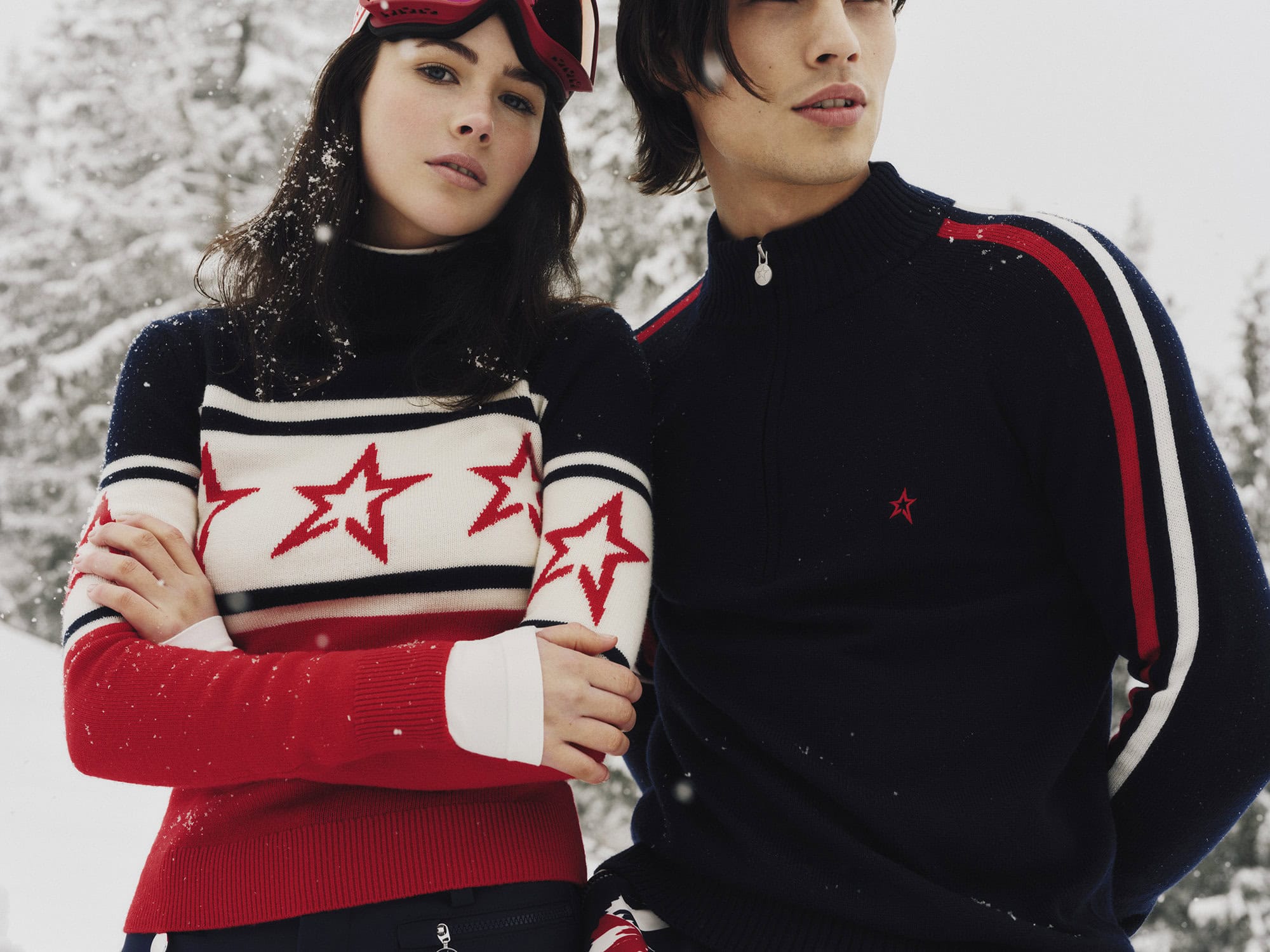 Two models wearing navy, white, and red star-patterned ski knitwear standing outdoors in a snowy landscape.