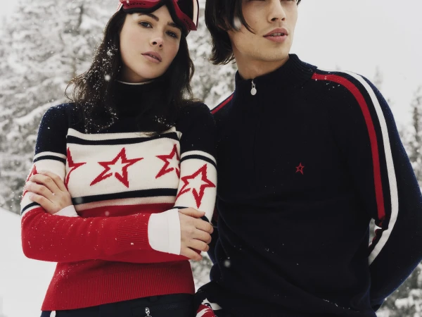 Two models wearing navy, white, and red star-patterned ski knitwear standing outdoors in a snowy landscape.