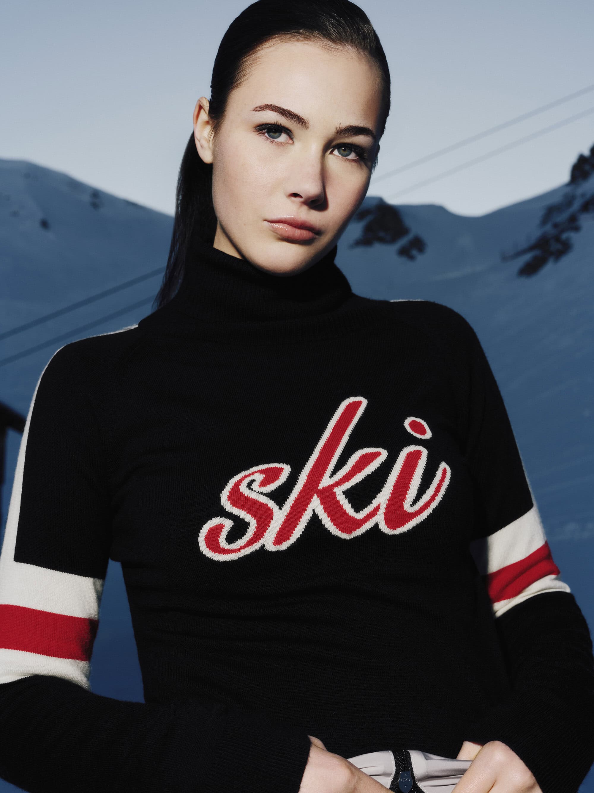 Model wearing a black turtleneck with red ski branding against a snowy mountain backdrop