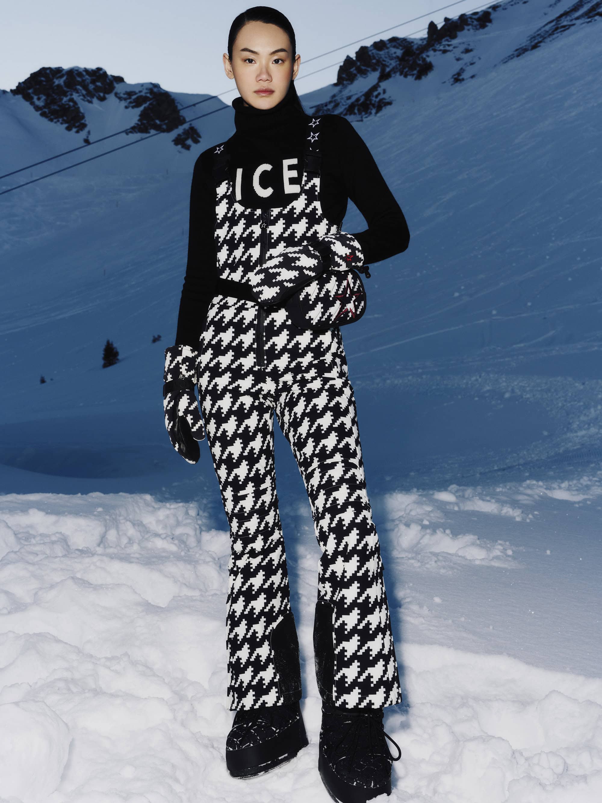 Model standing on snowy slope wearing black and white houndstooth ski suit and black turtleneck for Perfect Moment ad campaign