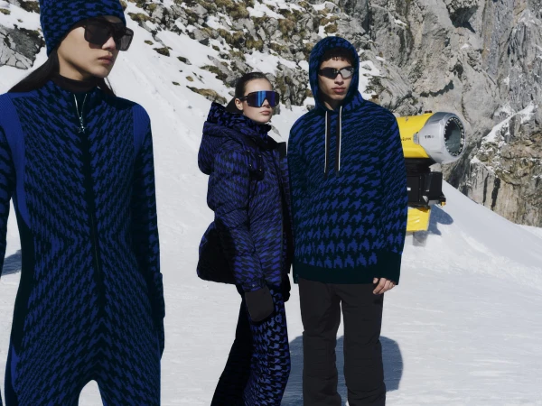 Three models wearing blue patterned winter ski apparel and sunglasses standing on a snowy mountain