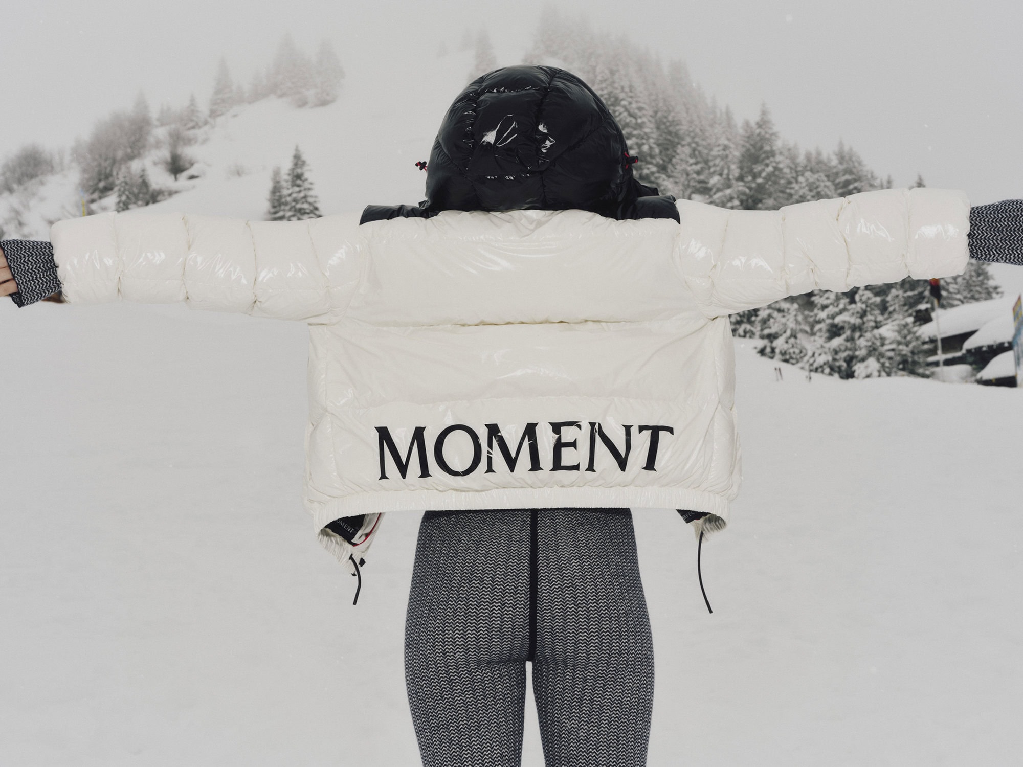 Rear view of a person wearing a white glossy puffer jacket with MOMENT branding outdoors in snow