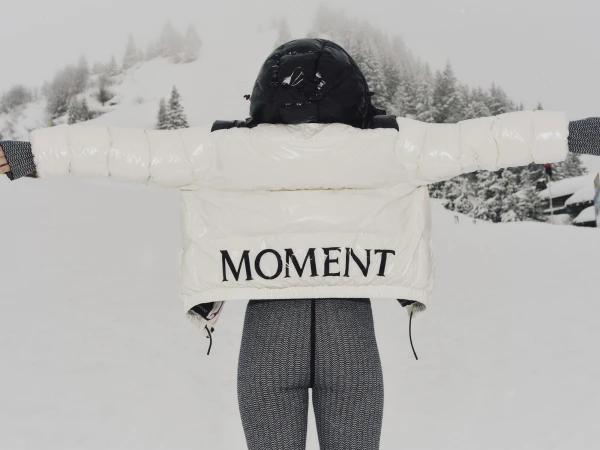 Rear view of a person wearing a white glossy puffer jacket with MOMENT branding outdoors in snow