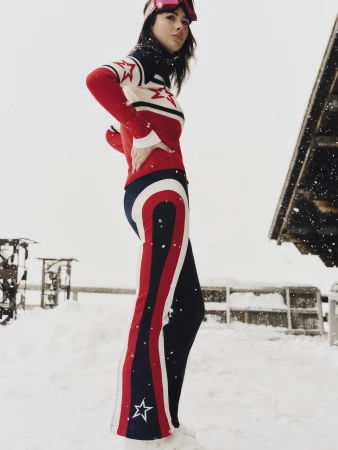 Model wearing red, white and blue ski apparel with star patterns posing outdoors in the snow