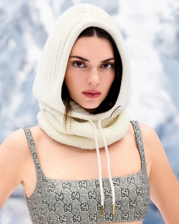 Kendall Jenner wearing a cream knit hood and patterned top against a snowy mountain backdrop for Gucci Holiday 2024 campaign