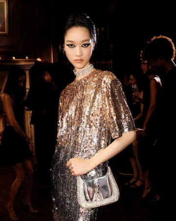 Model in glittering sequin dress wearing diamond choker holding a silver handbag in dim interior