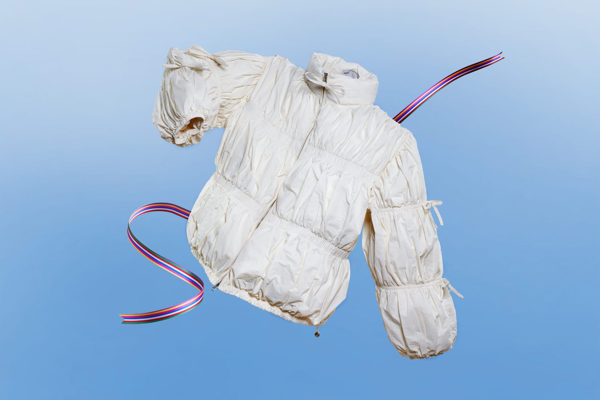 White puffer jacket with gathered sleeves floating against a gradient blue background with curving striped ribbons
