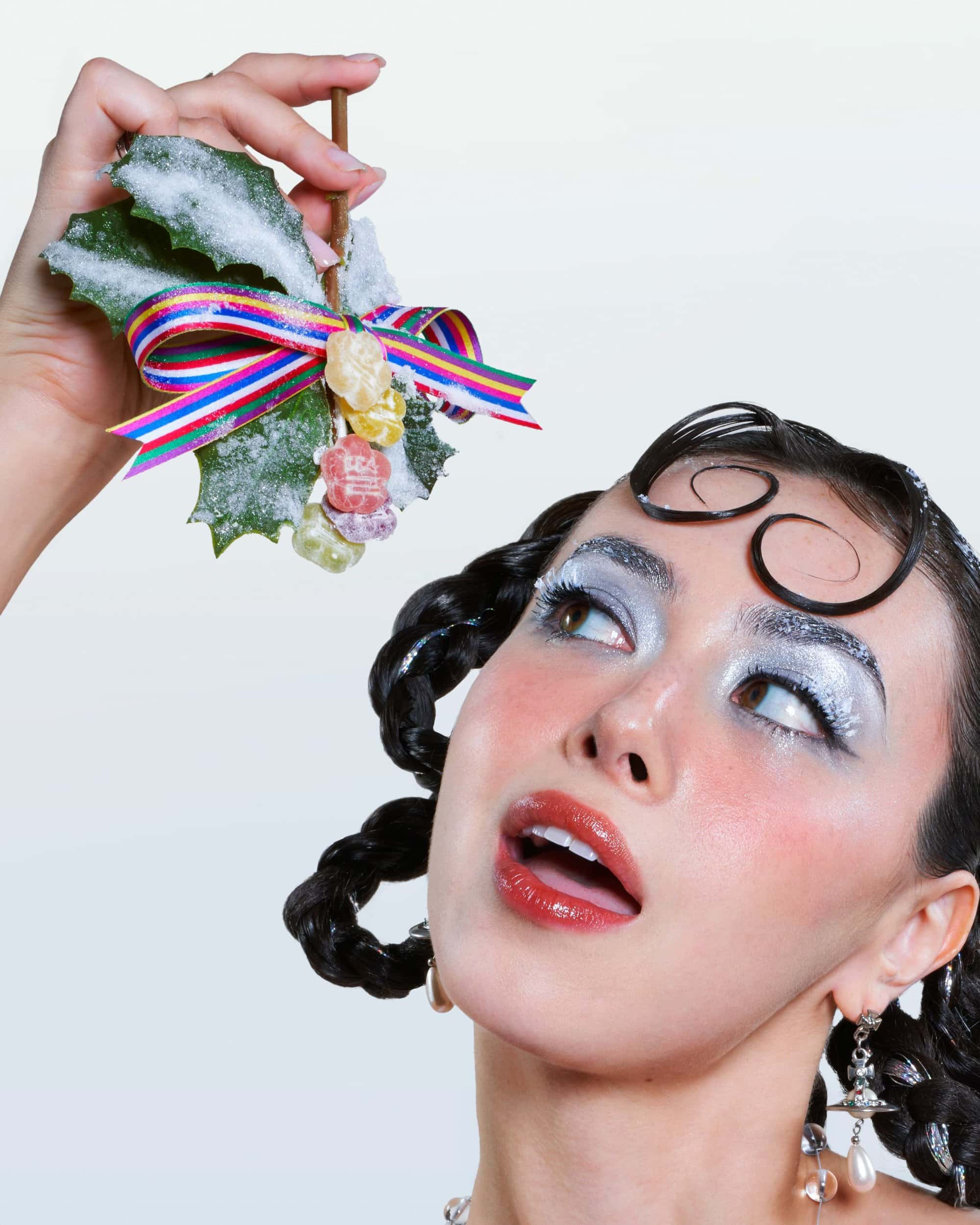 Model holding a sprig of frosted holly with gummy candy ornaments against a plain white background