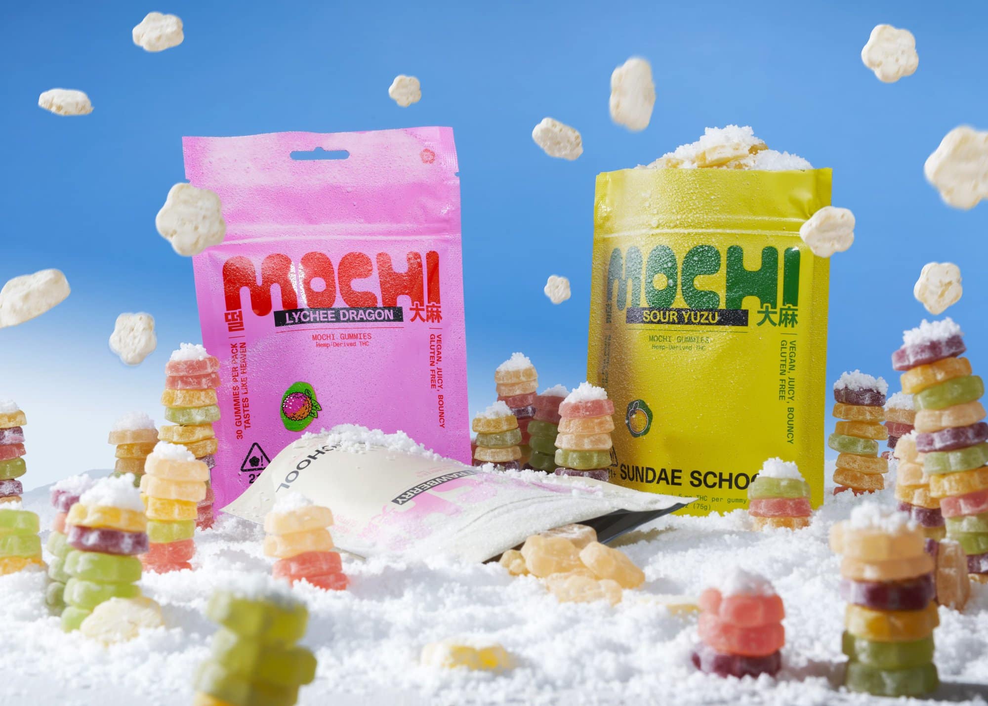Colorful candy pouches and stacked gummy candies surrounded by falling white flower-shaped pieces against a blue background