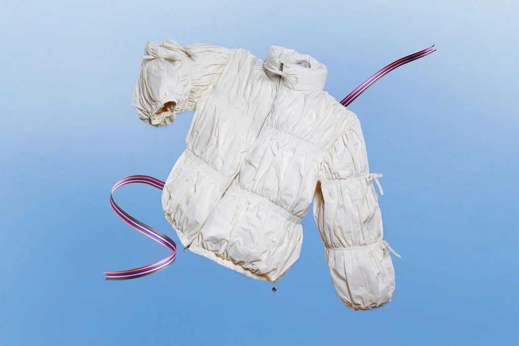 White puffer jacket with gathered sleeves floating against a gradient blue background with curving striped ribbons