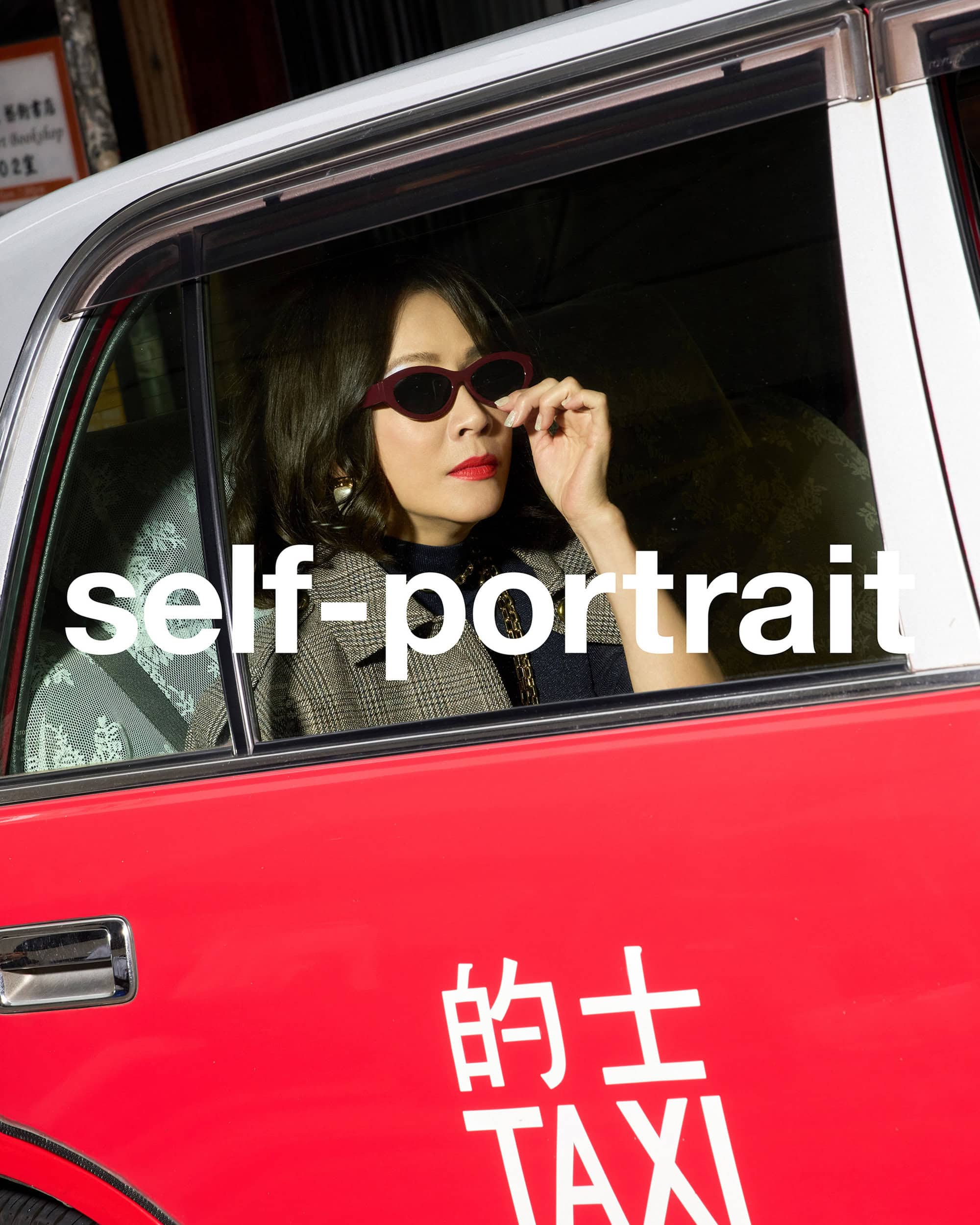 Woman in dark sunglasses and plaid coat sitting inside a red taxi cab