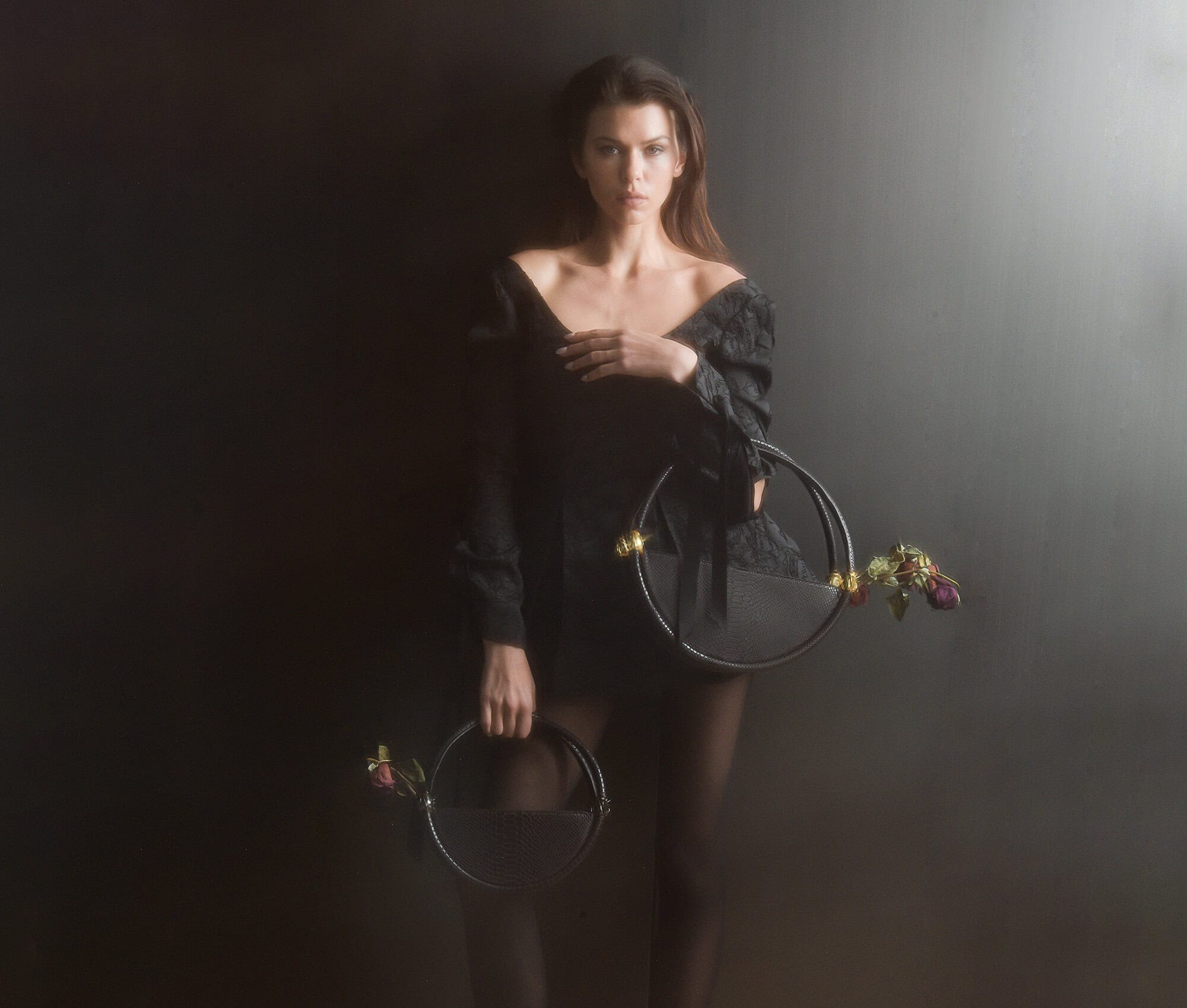 Model holding two circular black handbags against a dark studio background for Contessa Mills World Bag campaign