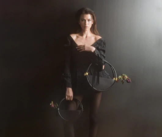 Model holding two circular black handbags against a dark studio background for Contessa Mills World Bag campaign