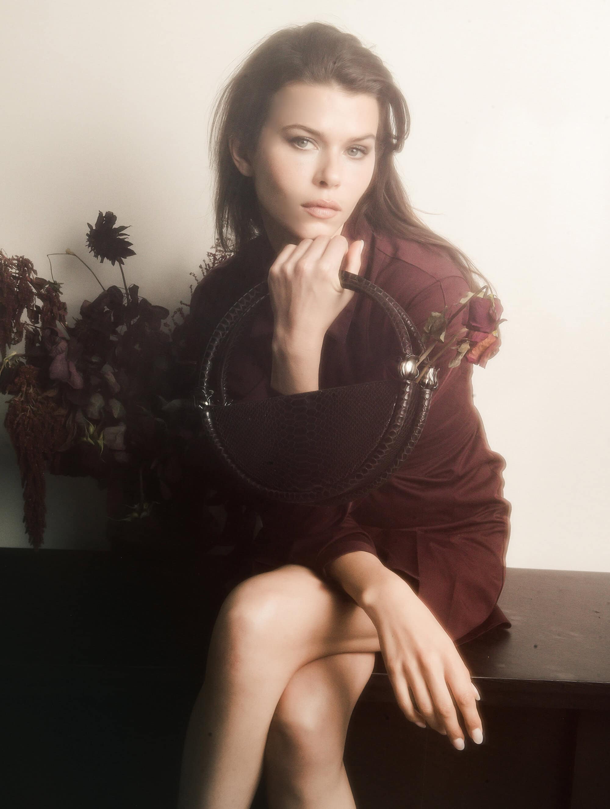 Georgia Fowler seated holding a dark handbag in the World Bag campaign by Contessa Mills