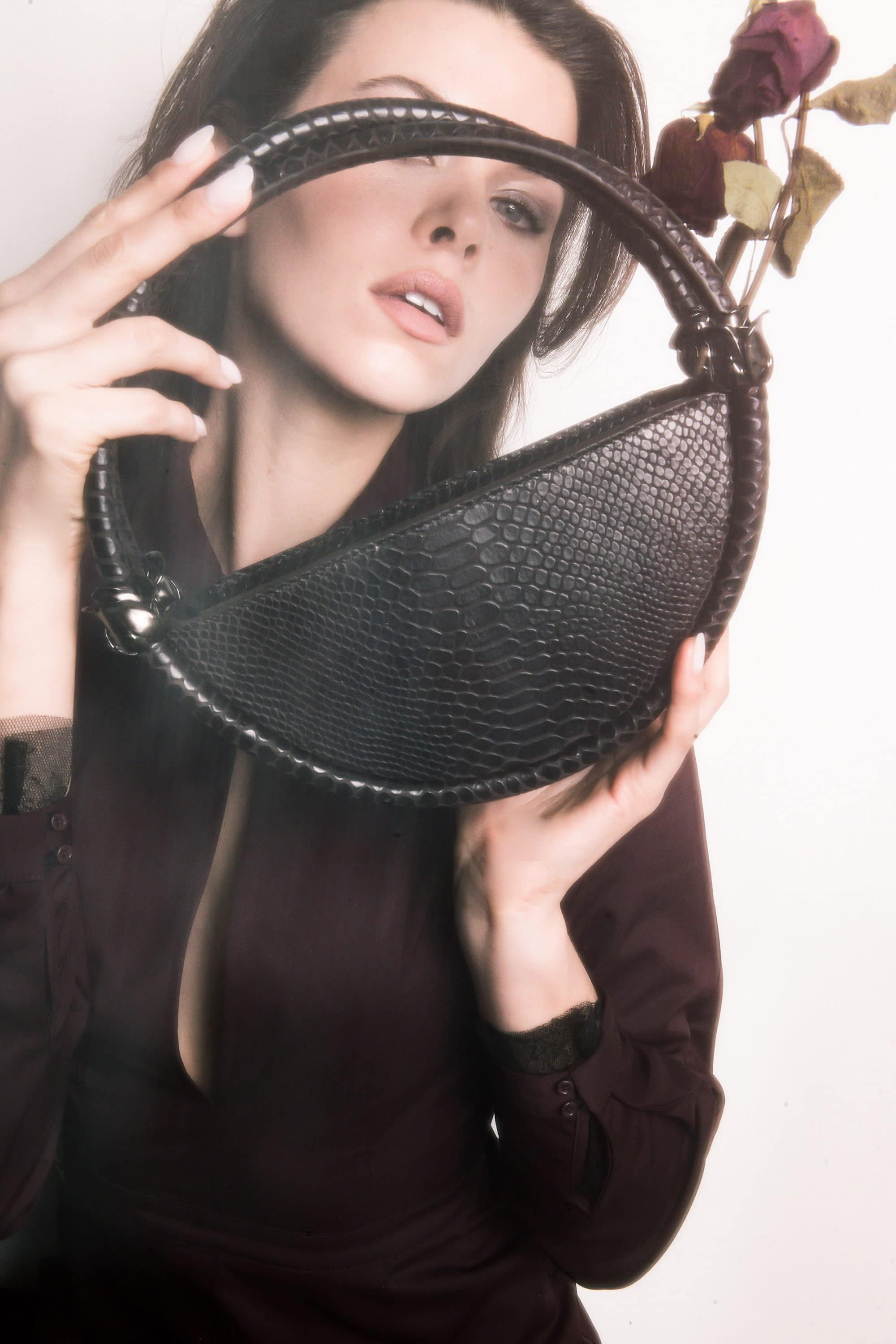 Model holding a black crescent handbag framing her face with dried roses for Contessa Mills World Bag campaign