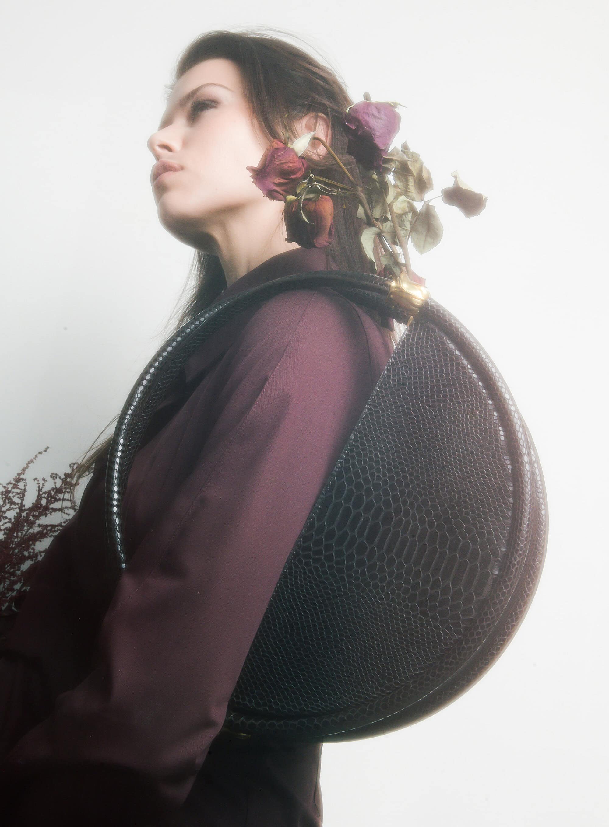 Georgia Fowler holding a structured black circular handbag filled with withered roses for Contessa Mills World Bag ad campaign.