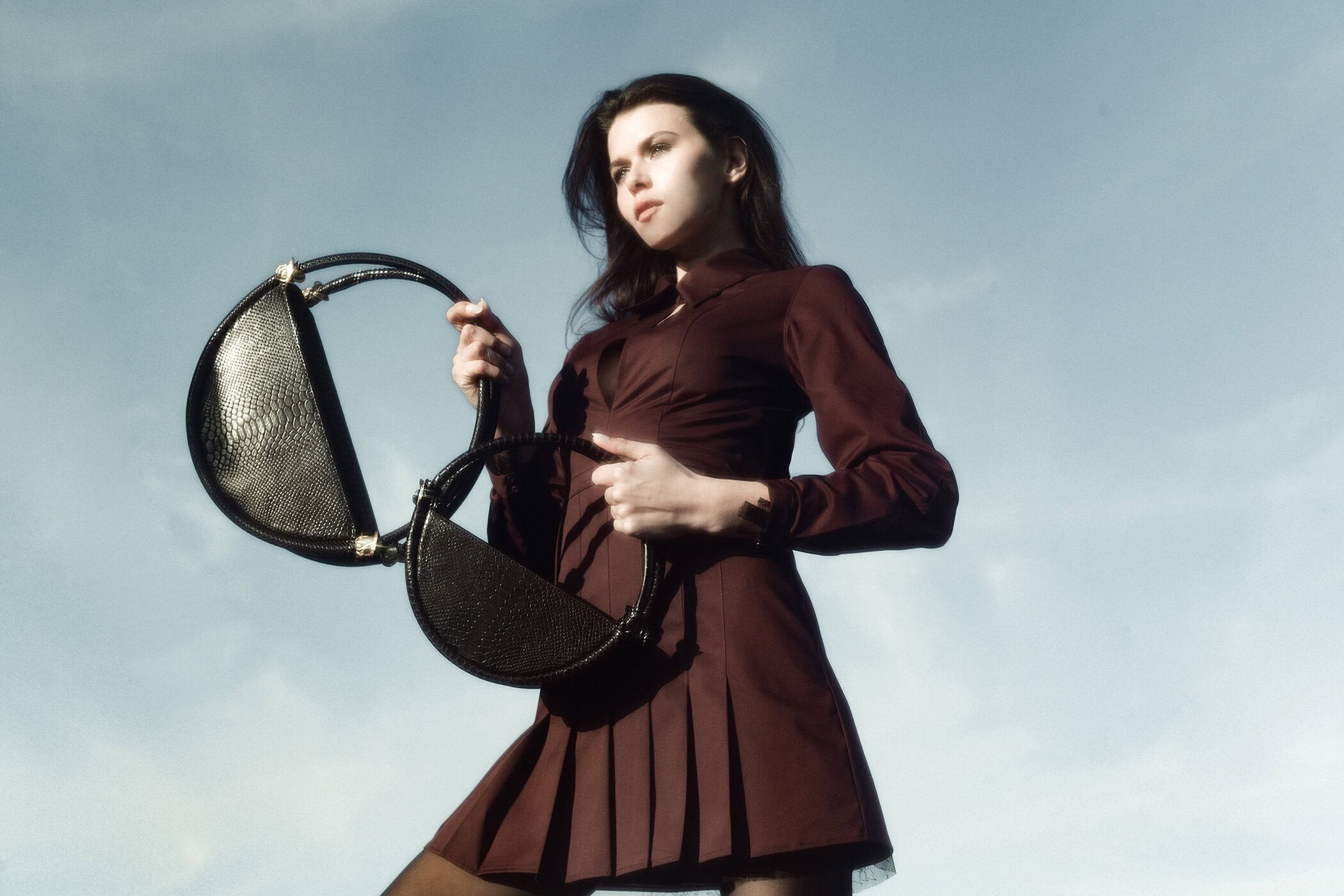 Model holding two structured black handbags against a clear sky background for Contessa Mills World Bag campaign
