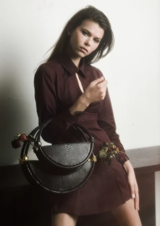Model wearing a dark burgundy dress holding a textured black handbag against a neutral background.