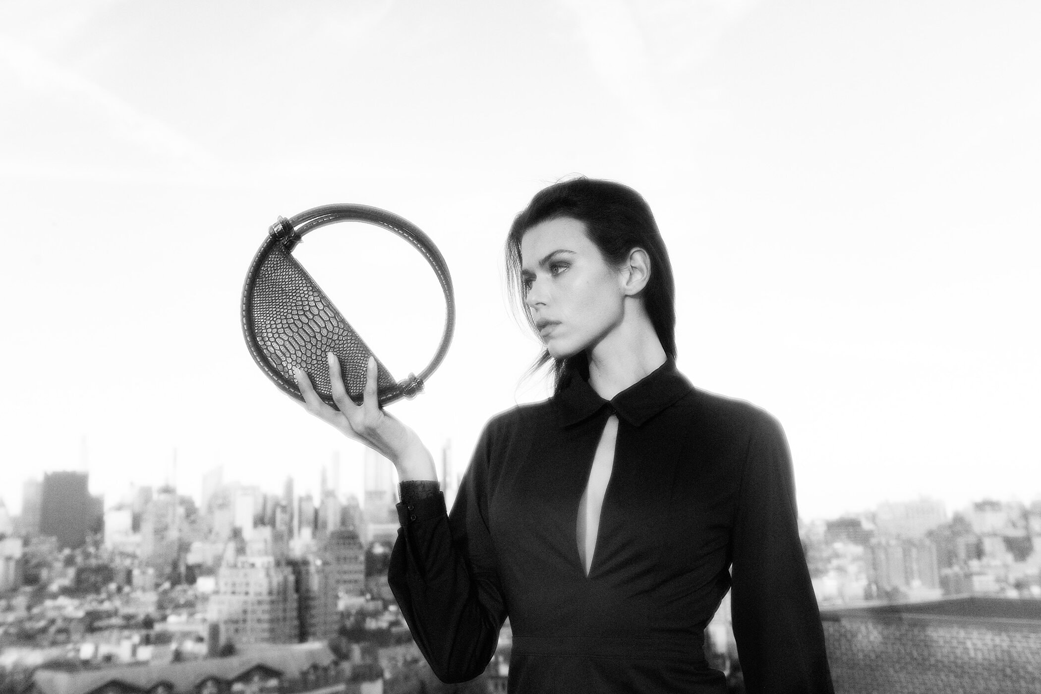 Model Georgia Fowler holding a circular textured handbag against a city skyline for Contessa Mills World Bag campaign