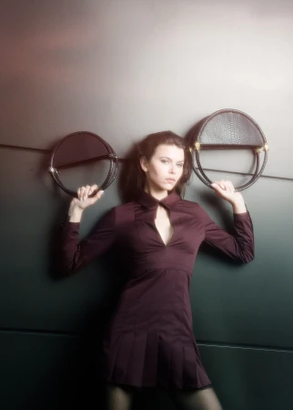 Model Georgia Fowler posing against a dark wall holding two round black leather handbags for Contessa Mills