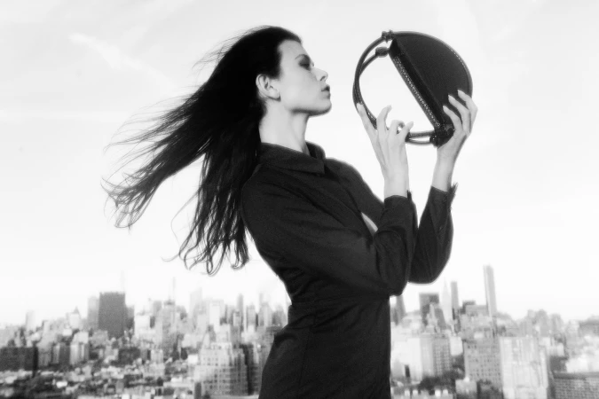 Model Georgia Fowler holding a circular handbag against a city skyline for Contessa Mills World Bag campaign