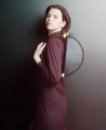 Model in a burgundy dress holding a black textured round handbag against a dark gradient background