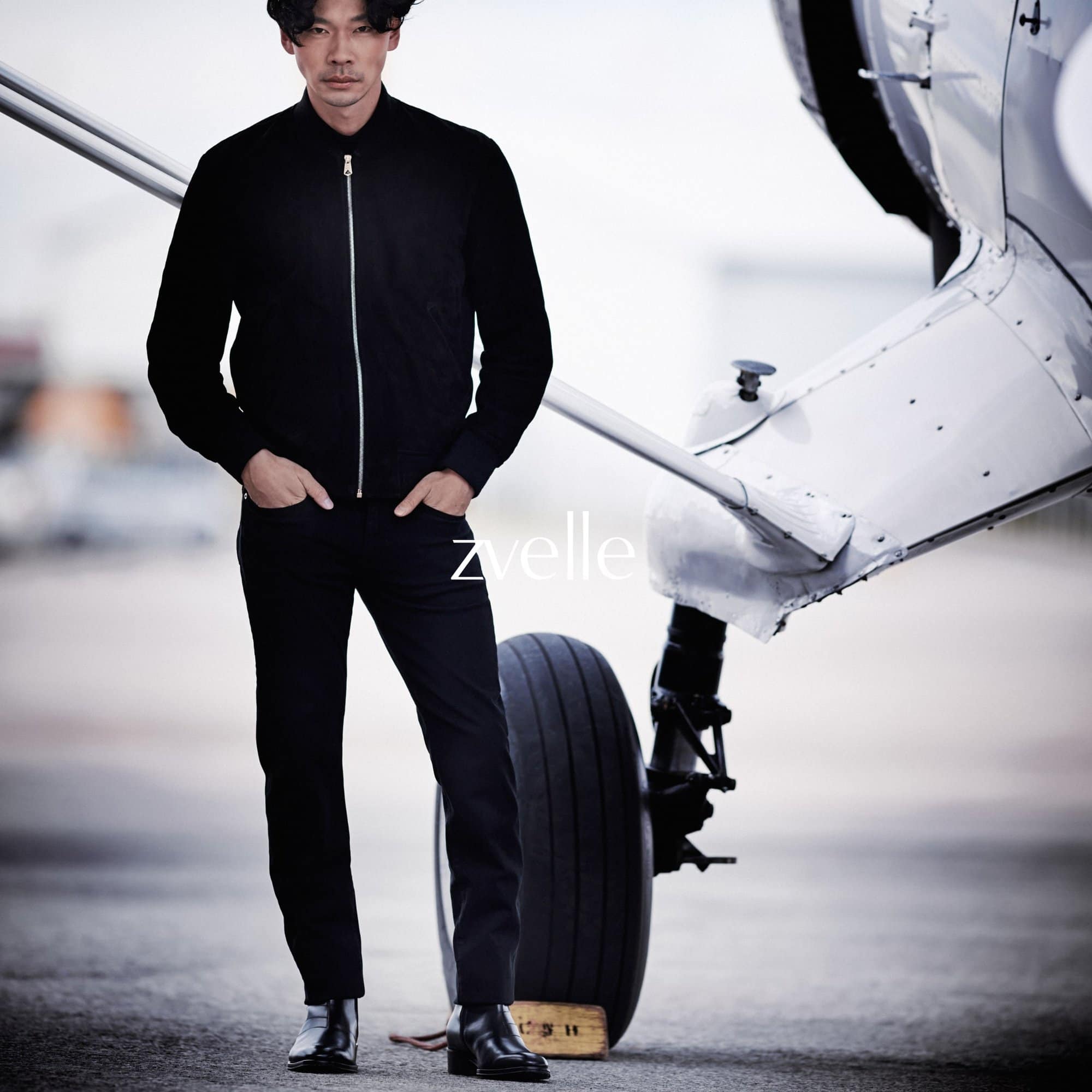 Man wearing a black zip jacket and black trousers standing next to a small aircraft wheel for Zvelle Alatus campaign